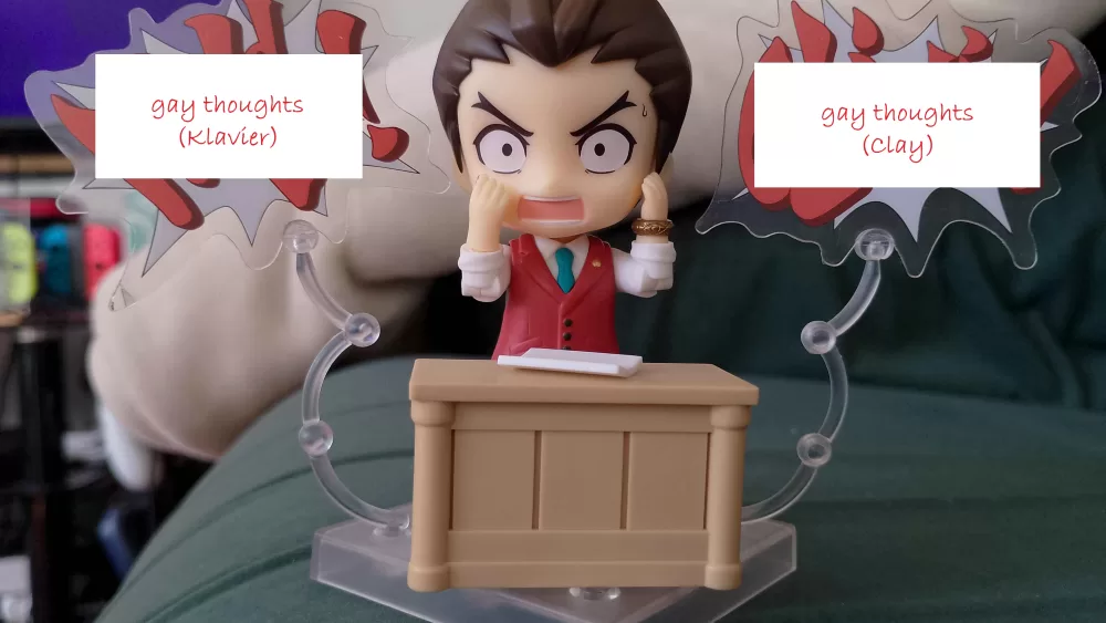 Apollo Justice Ace Attorney in Nendoroid form wrestles with his gay thoughts in the form of badly-photoshopped speech bubbles shouting out his barely-subtextual homoerotic feelings about Clay and Klavier. There's also a fetching cameo from Rebecca's ancient (but sooo comfy) green sofa.